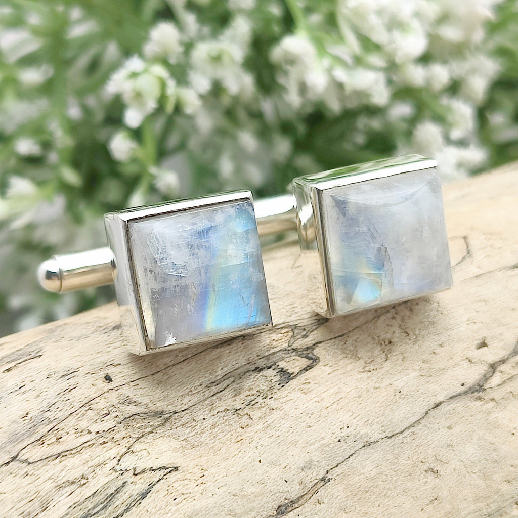 Moonstone cufflinks on driftwood with white flowers in the background