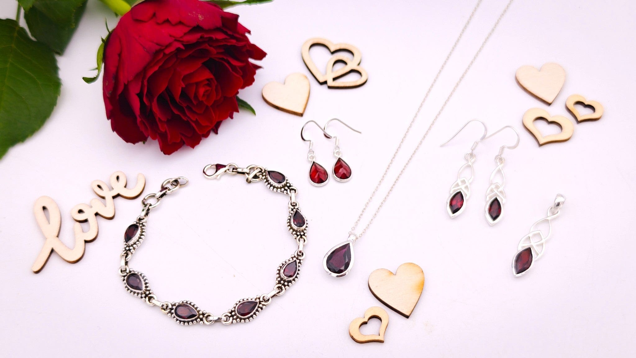 Garnet gemstone jewellery on a pale background with a red rose in the top corner