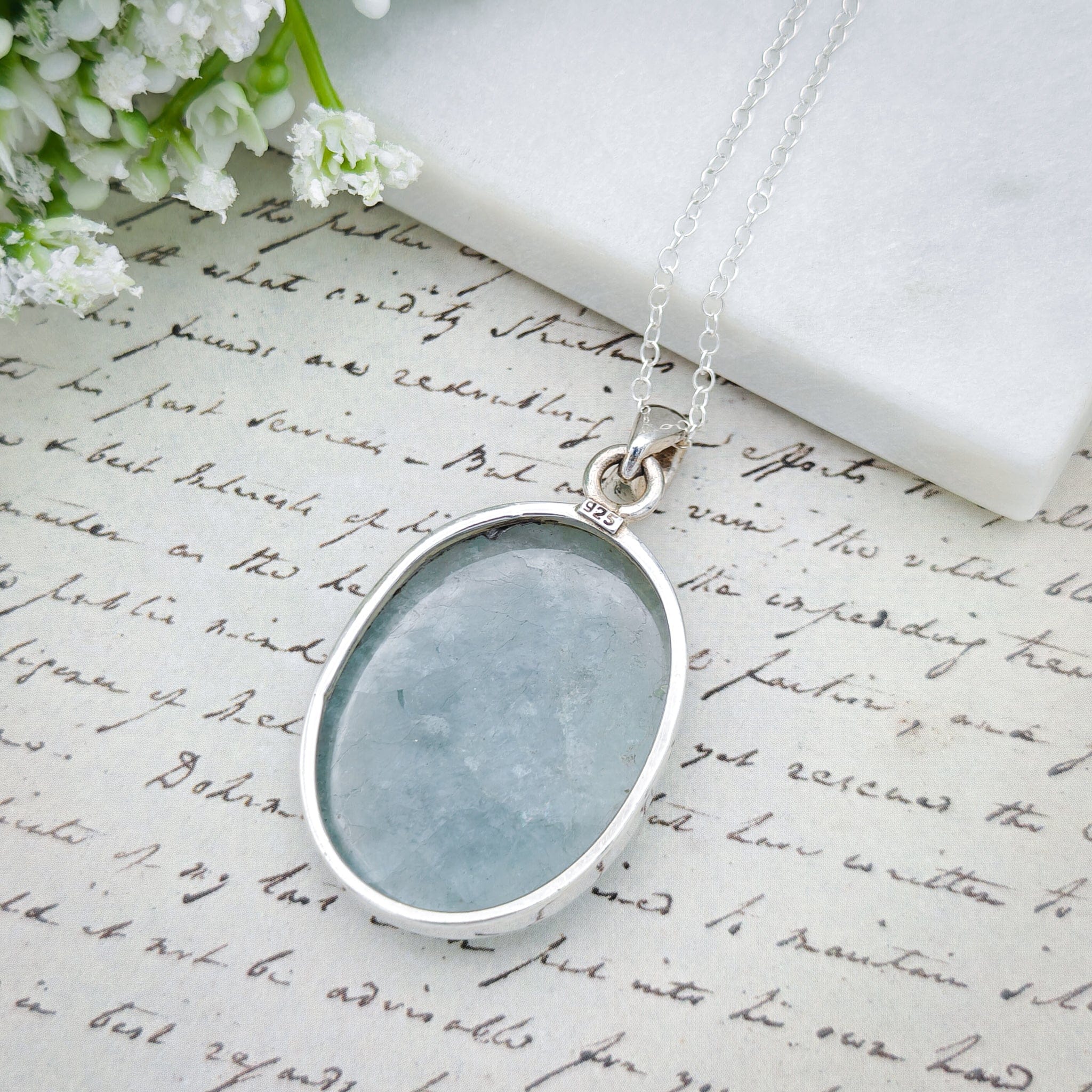Hepburn and Hughes Aquamarine Sterling Silver Pendant, showing the back of the stone and the silver band, on antique paper