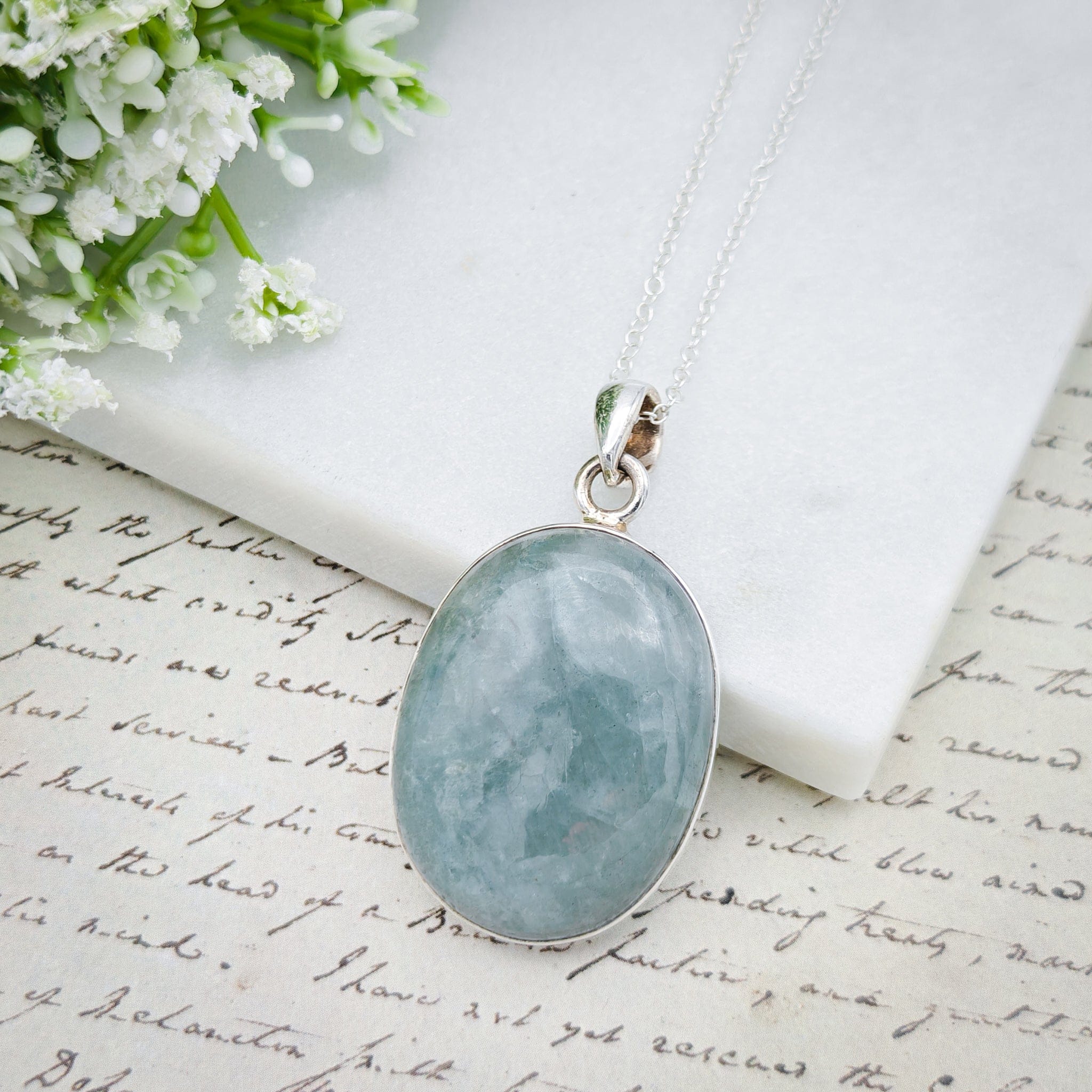 Hepburn and Hughes Aquamarine Sterling Silver Pendant, styled with chain on a pale background with antique paper background and flowers in the corner