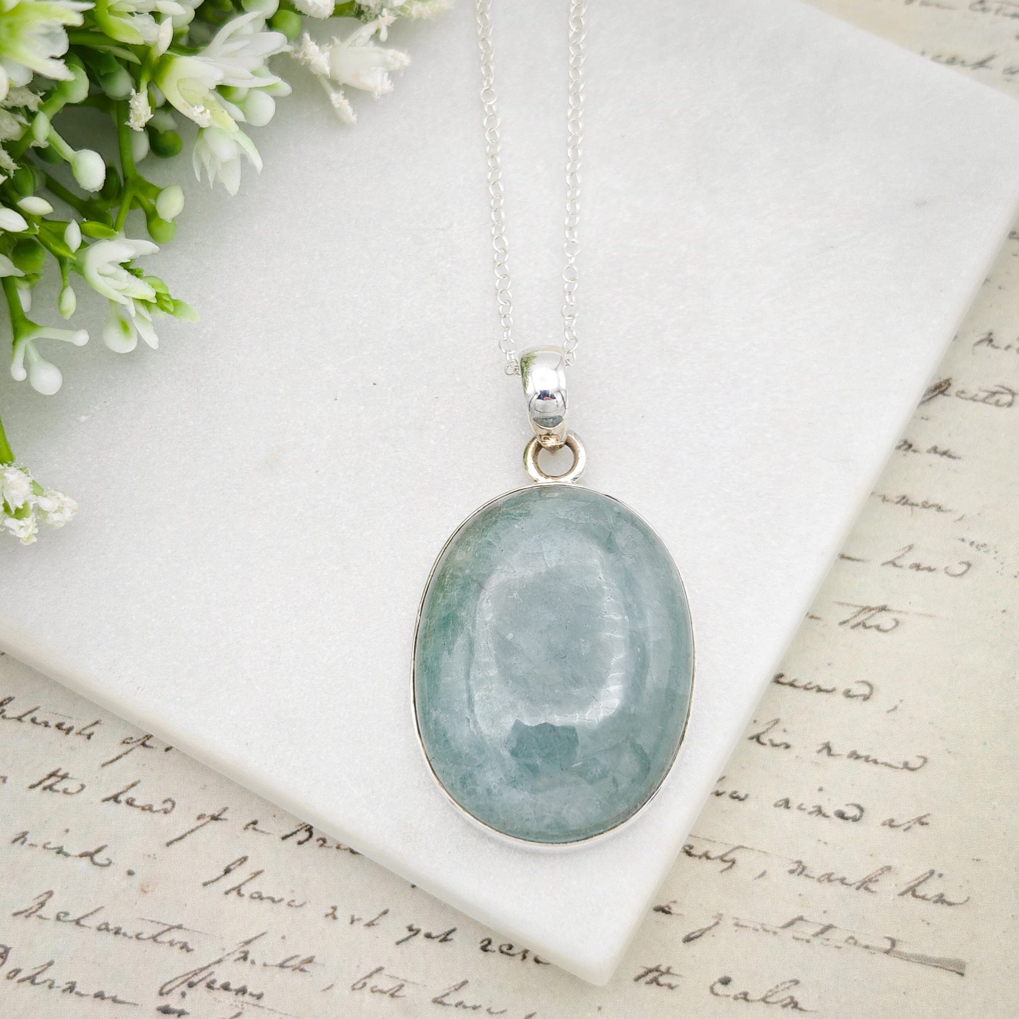 Hepburn and Hughes Aquamarine Sterling Silver Pendant on pale background with flowers in the corner. Set on a silver chain
