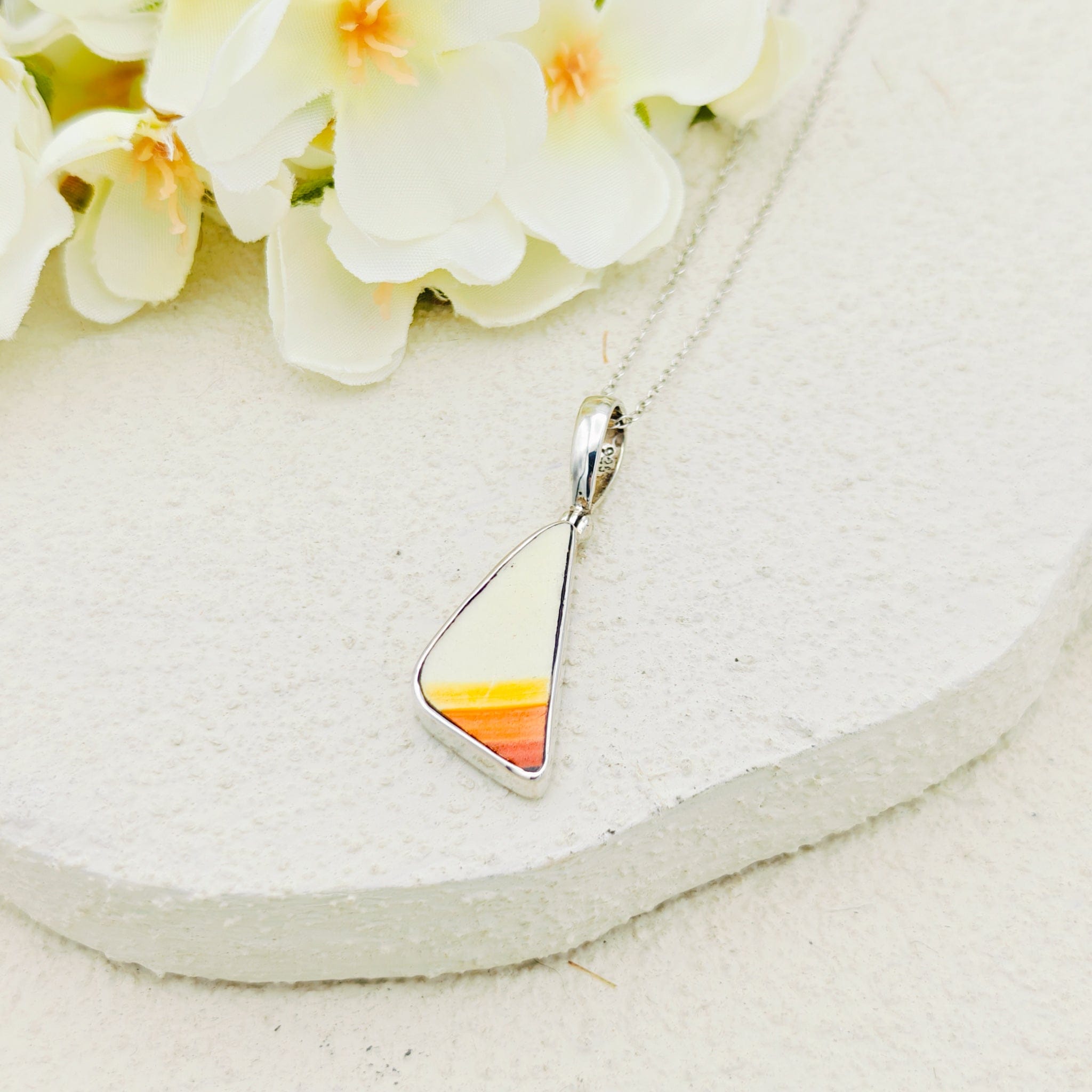 Hepburn and Hughes Original Clarice Cliff Pottery pendant Triangle in orange, yellow and white stripes. Sterling Silver with a silver chain on a white stone background with orchids in the top corner