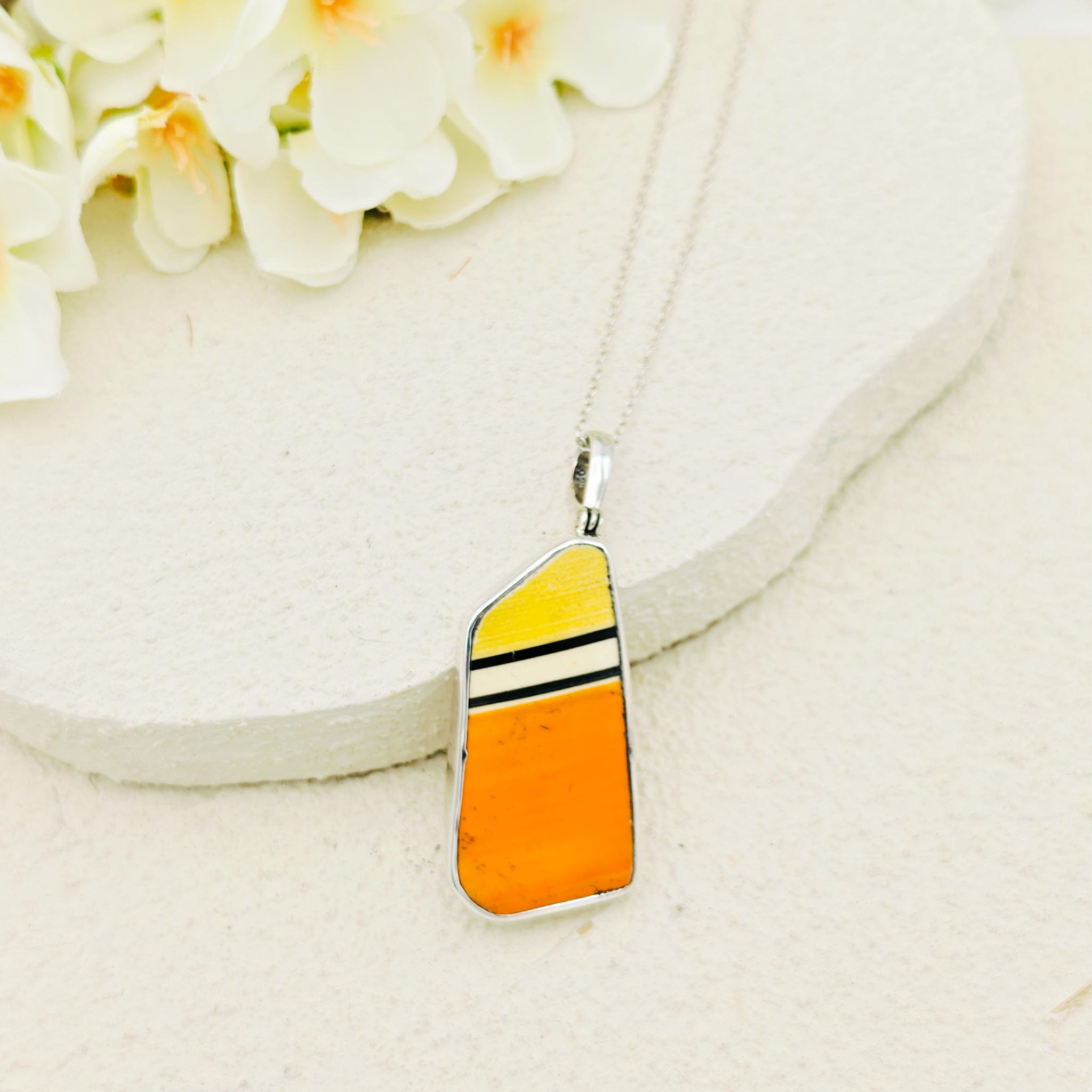Clarice Cliff Necklace with a yellow and orange pendant on a white background, silver chain and flowers above